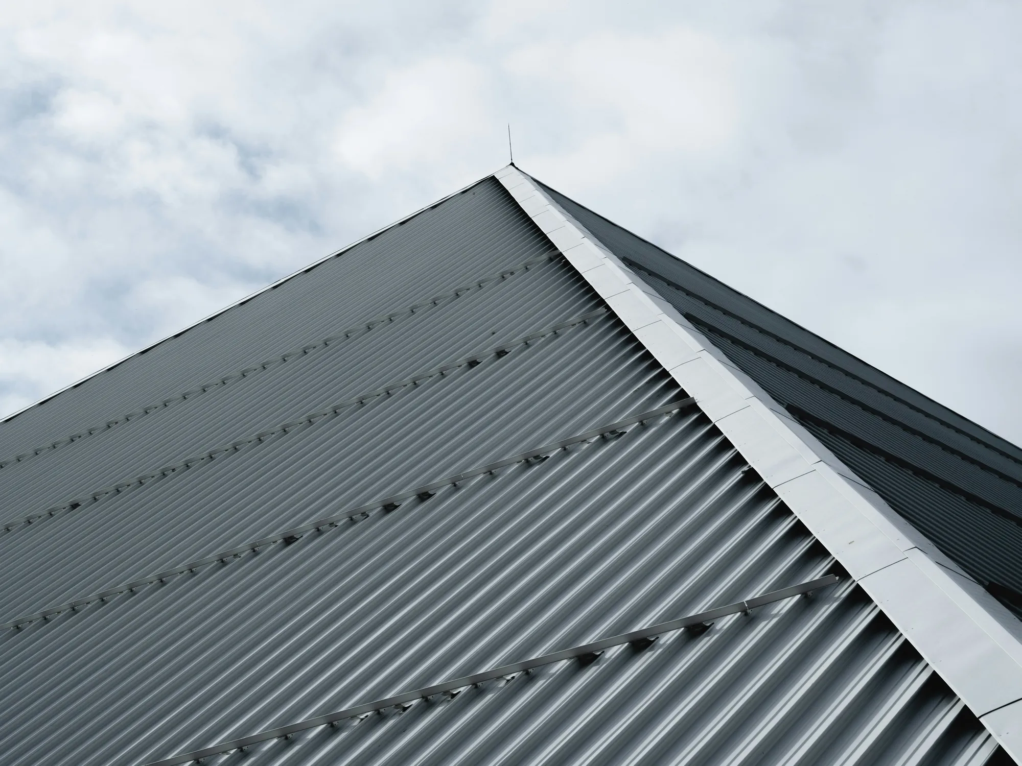 A grey ribbed metal roof rising to a peak against a cloudy sky